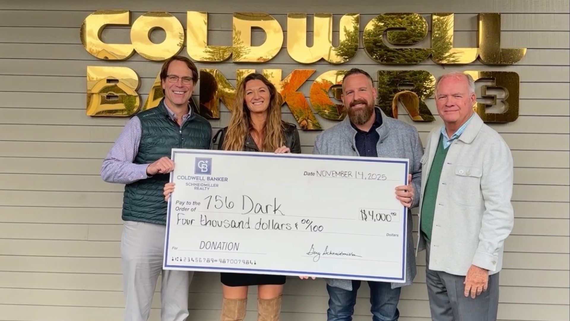 Schneidmiller Realty leadership holding a large donation check for 756 Dark
