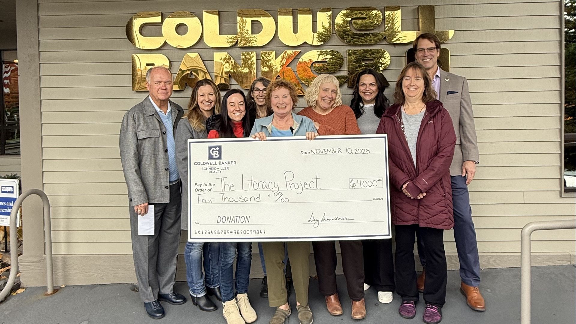 Schneidmiller Realty leadership holding a large donation check for The Literacy Project