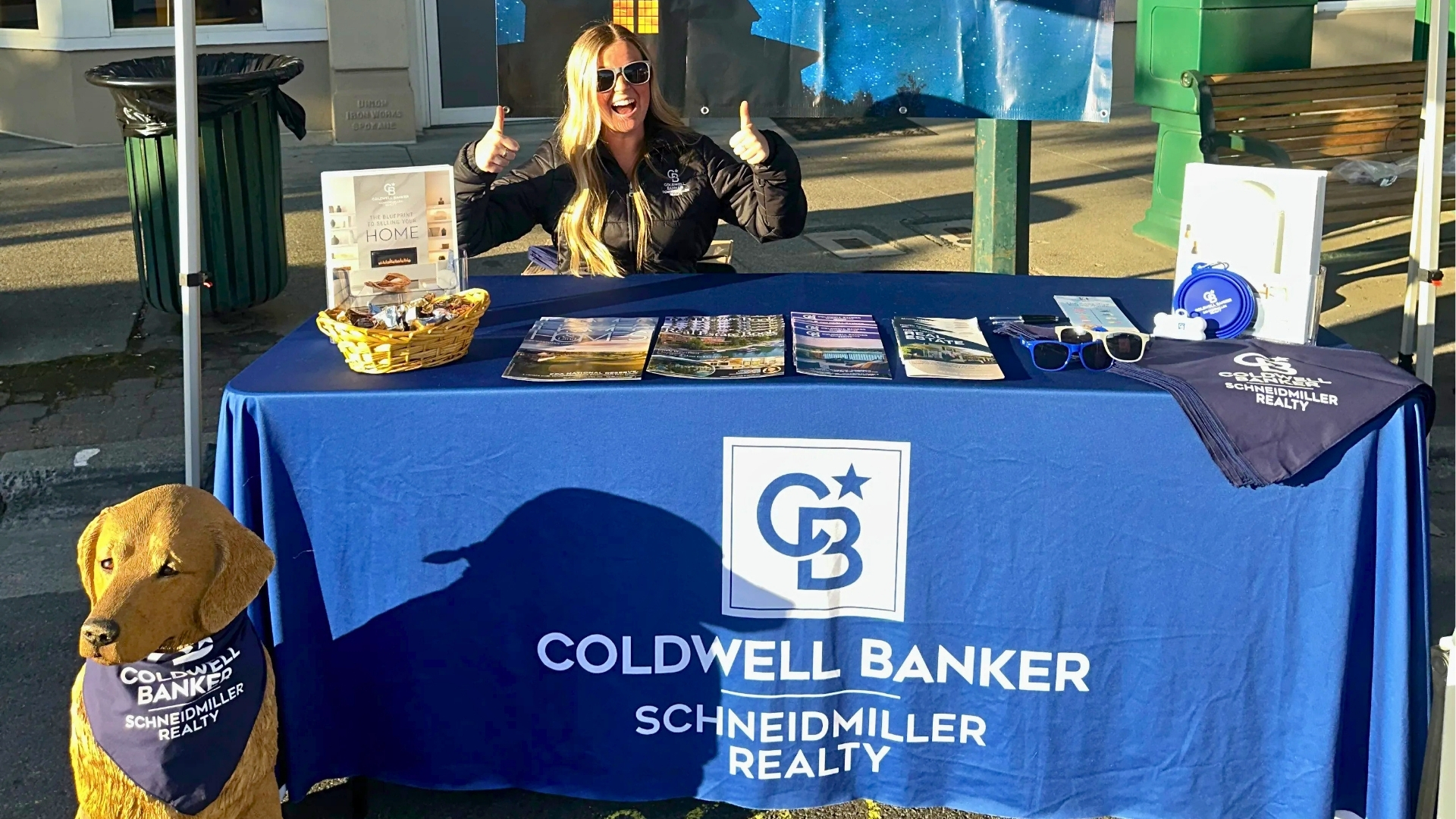 Team member giving two thumbs up behind the Coldwell Banker Schneidmiller Realty table